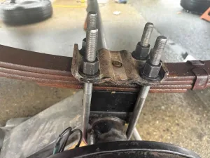 8. Install the new U-bolts through the tie plate and tighten the nuts to the specified torque.